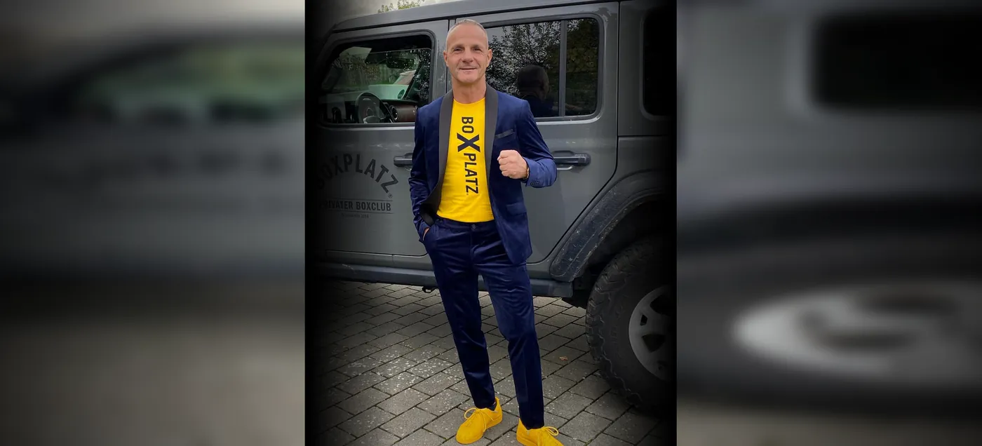 Mario Dimitroff im blauen Anzug mit gelbem Boxplatz-Shirt vor dem Boxplatz-Fahrzeug